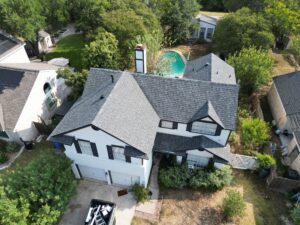 Aerial view of a Central Texas home with a dark asphalt roof and backyard pool in late summer
